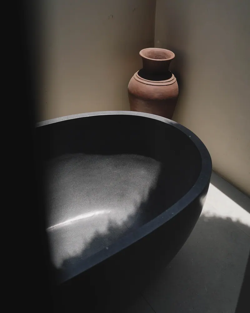 Close view of a dark stone bathtub with a clay vase