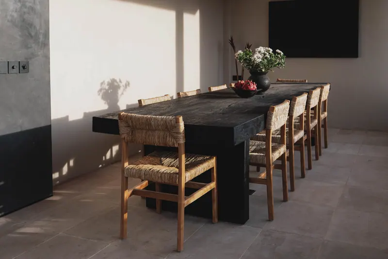 Long dark dining table with woven chairs in morning light