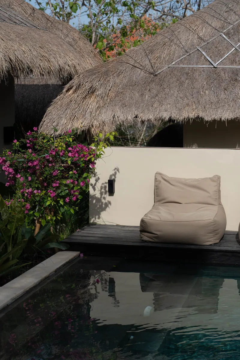 Bean bag lounger beside the pool under a thatched roof, with bougainvillea