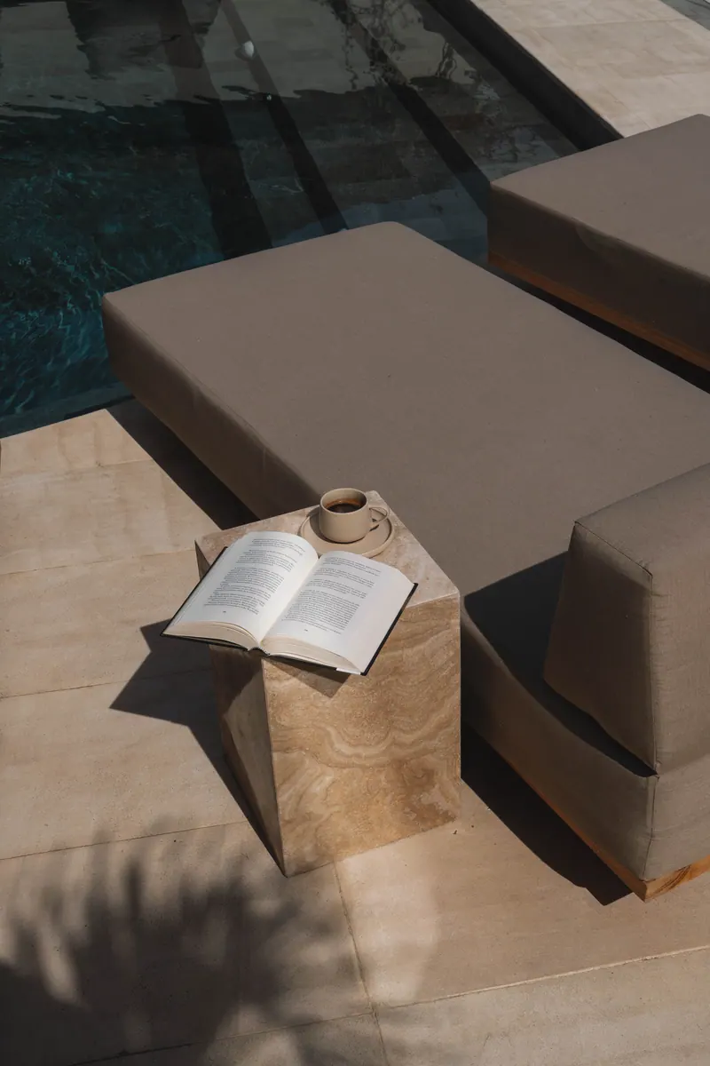 Open book and coffee on a stone side table by the pool
