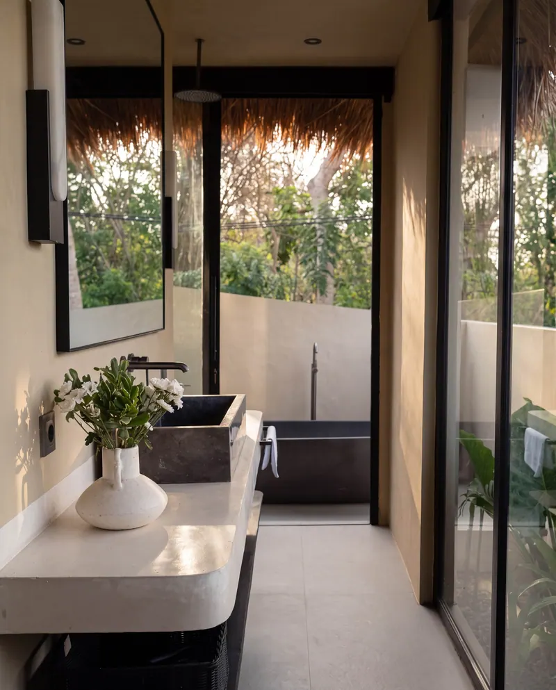 Stone basin and freestanding bathtub beside glass doors to the garden