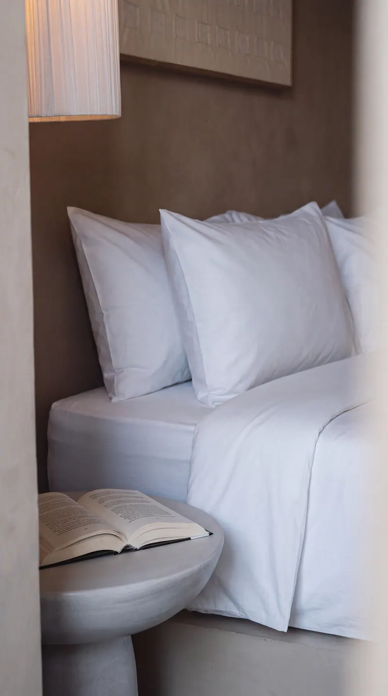 Bed with white linen and a book on a stone side table
