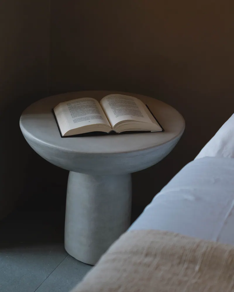 Stone side table with an open book beside the bed