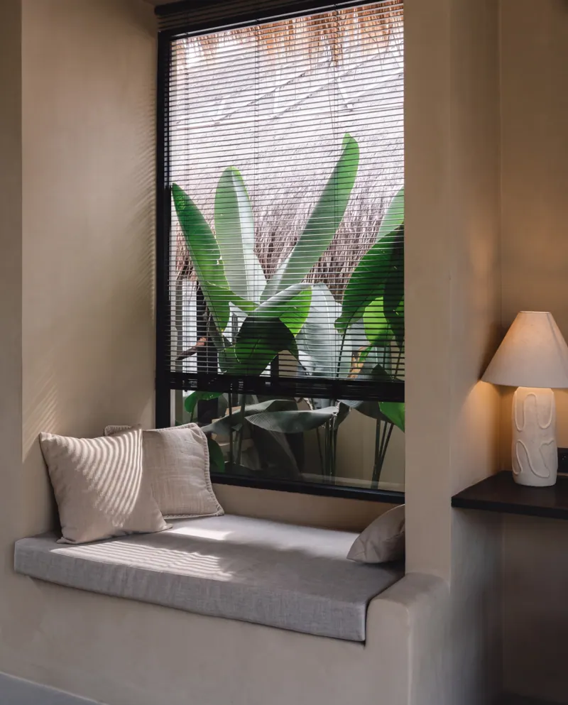 Window seat with cushions and a lamp, looking onto tropical leaves